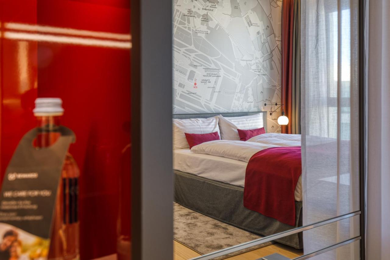 Intercityhotel Berlin Airport Ber Terminal 1 & 2 Schönefeld Exteriör bild The photo shows a modern hotel room that features a comfortable bed with white linens and a red accent blanket. Behind the bed is a stylish wall displaying a map design. The room has large windows dressed with light-colored curtains, allowing natural